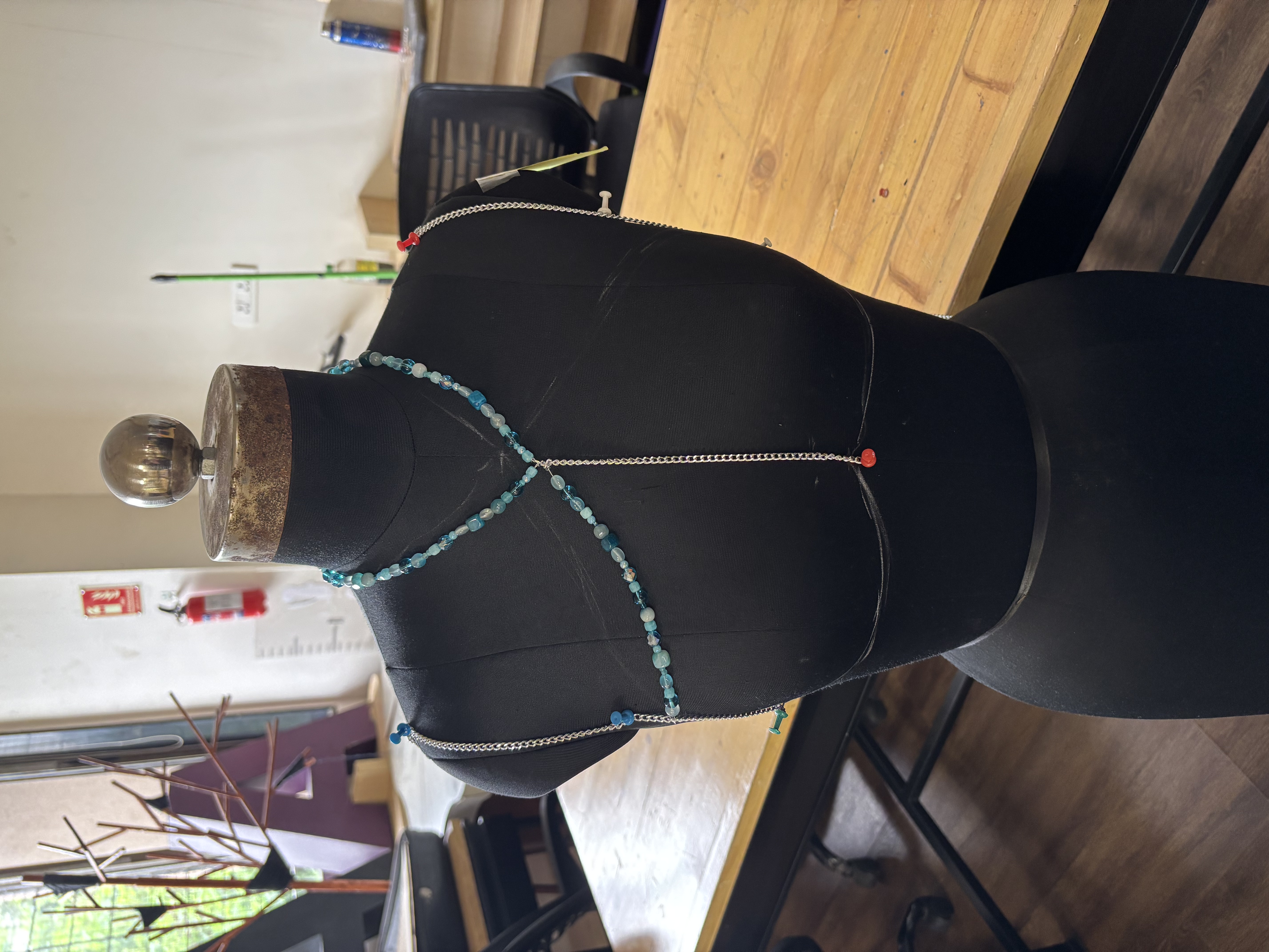 Early stage of the beaded garment, a single strand of beads pinned across a mannequin