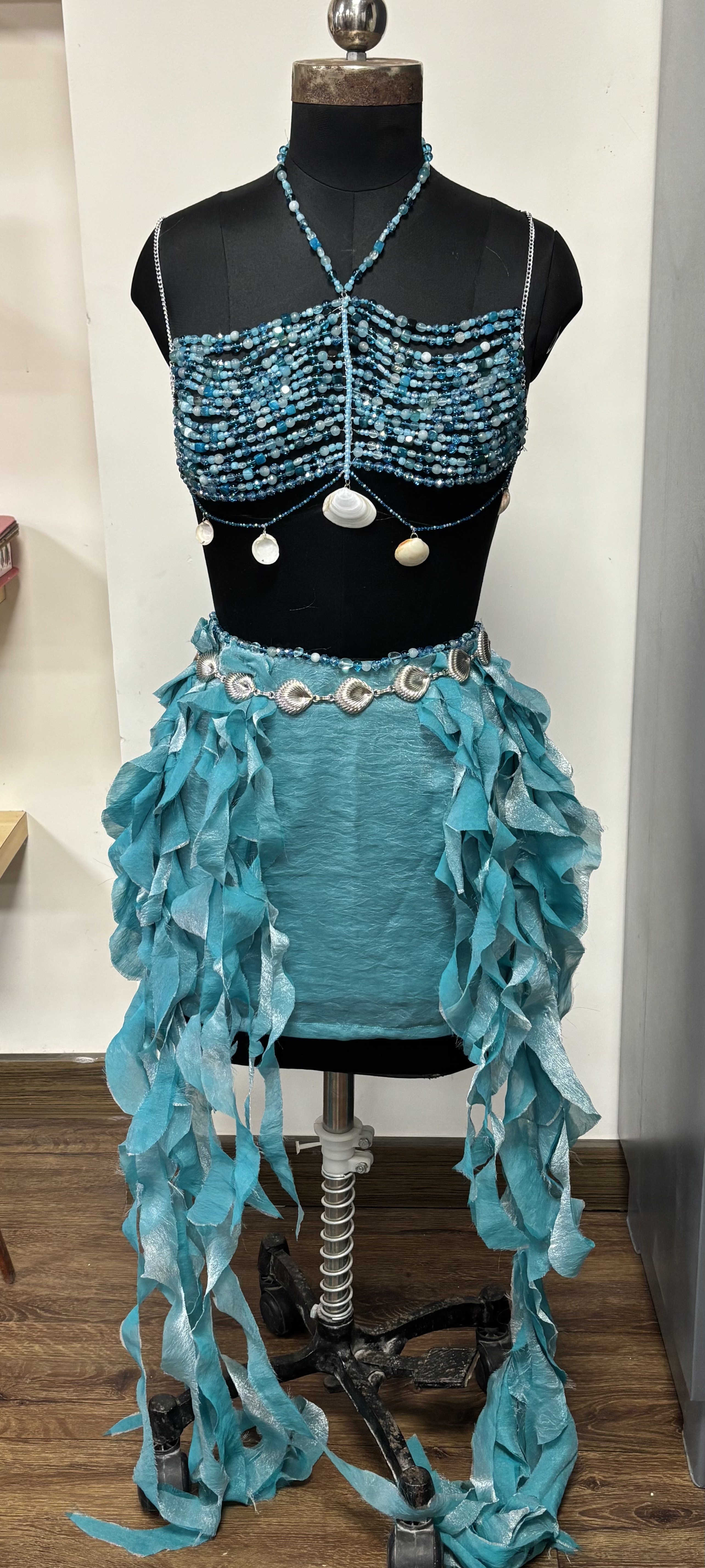 The finished garment on a mannequin: a beaded halter top with shell details and a flowing teal frilled skirt