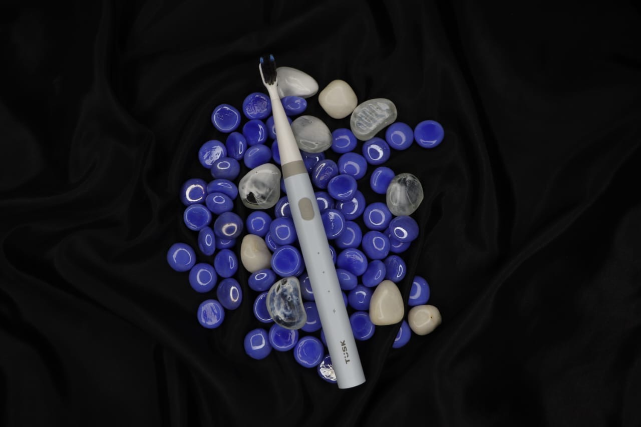 TUSK toothbrush resting on cobalt-blue glass pebbles under warm light, an early prop and texture exploration