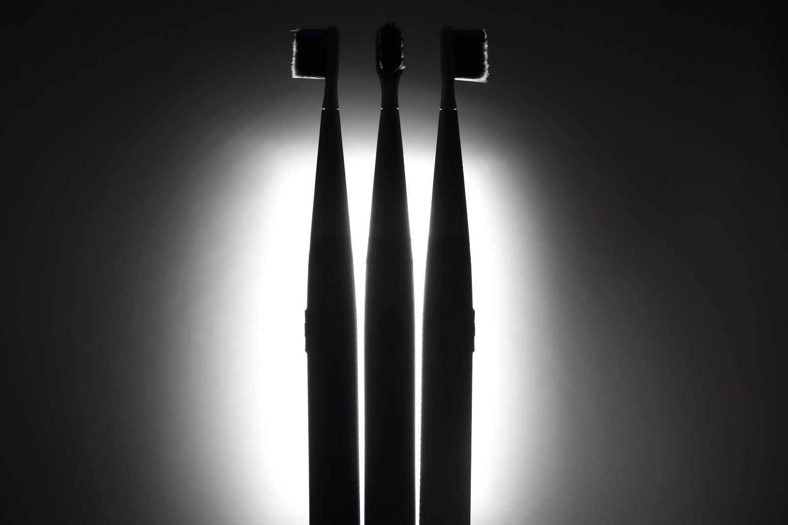 Three TUSK toothbrushes backlit in silhouette against black, representing the dark charcoal concept
